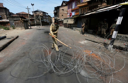 A policeman uses a stick to adjust concertina wire as he lays a barricade on a road during a curfew in Srinagar, August 6, 2016. REUTERS/Danish Ismail