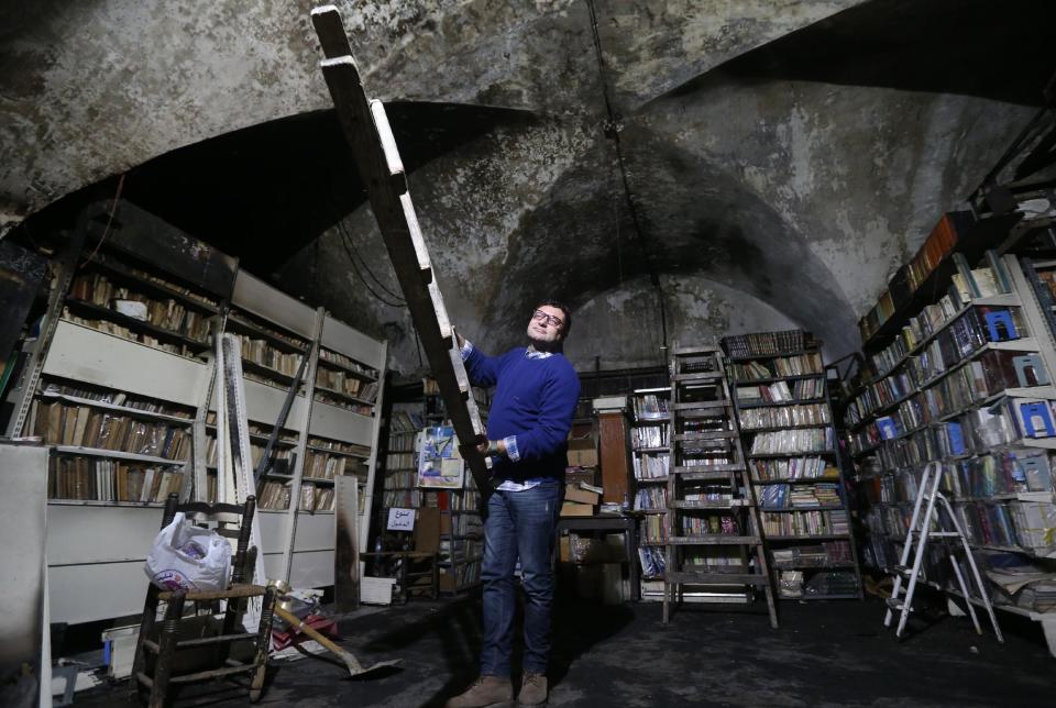 In this picture taken on Sunday, Jan. 5, 2014, a Lebanese activist carries a wooden ladder as he cleans the Saeh (Tourist) Library which was set on fire by masked men, in the northern city of Tripoli, Lebanon. Books that were burnt in an arson attack targeting a crammed, chaotic and popular library in the northern Lebanese city of Tripoli have become the latest victim of the country's rising sectarian tensions.(AP Photo/Hussein Malla)