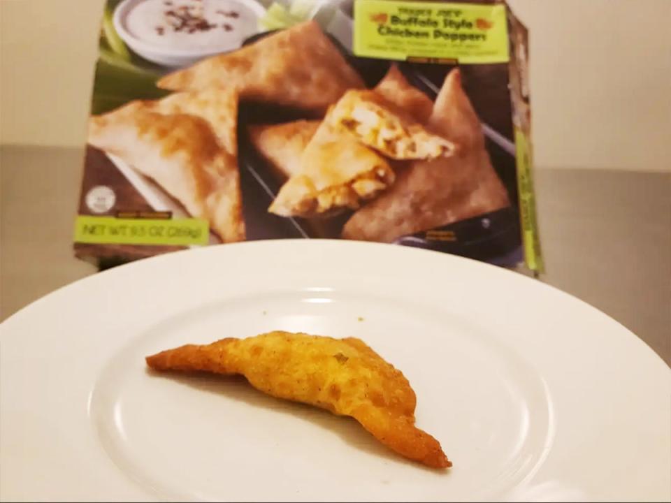 A golden-brown chicken popper on a white plate in front of a green box of chicken poppers