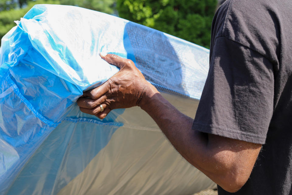 A man lifts one end of a covered mattress in the process of moving it.