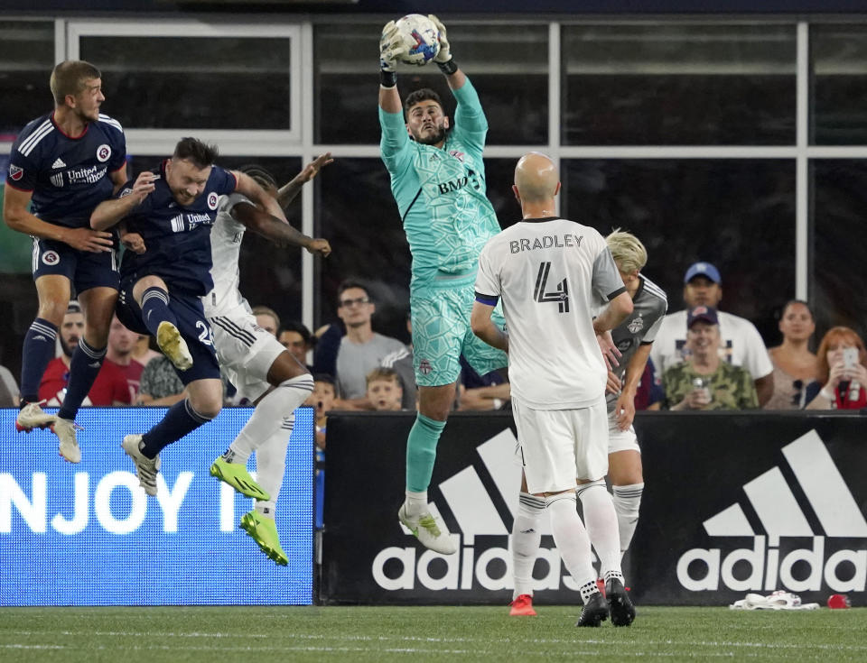 Toronto FC goalkeeper Alex Bono (25) leaps to make as save in front of New England Revolution players during the first half of an MLS soccer match Saturday, July 30, 2022, in Foxborough, Mass. (AP Photo/Mary Schwalm)