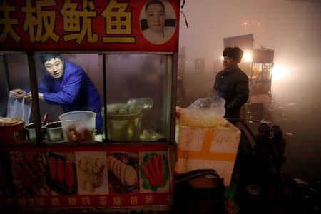 FILE PHOTO: A street food vendor prepares food for customers as heavy smog blankets Shengfang, in Hebei province, on an extremely polluted day with red alert issued, China December 19, 2016. REUTERS/Damir Sagolj/File Photo