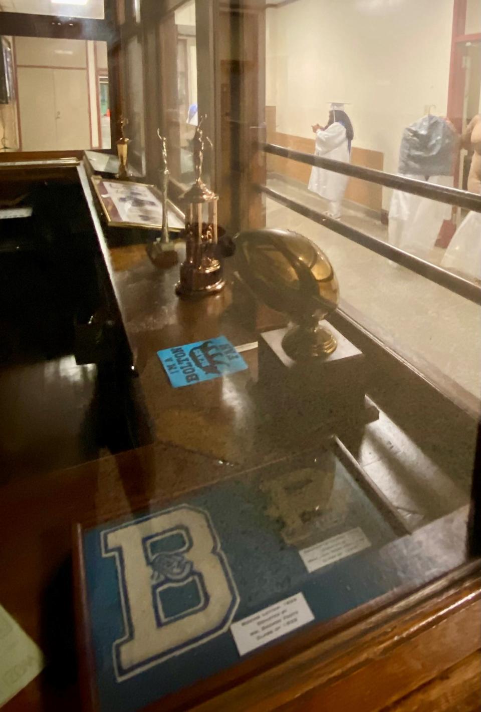 Celie Hillman can be seen looking at her phone through a display case of Bolton High School honors from years past. Hillman is among the last class of Bolton graduates before the school transforms into an academic and performing arts magnet.