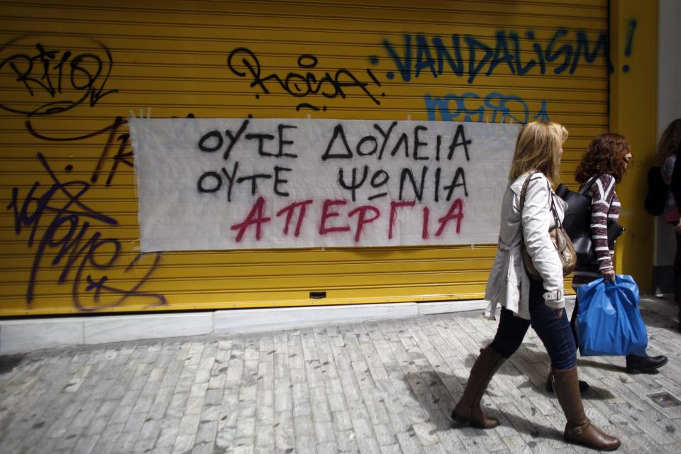 Pedestrians walk in front of a closed shop with a banner that reads "No Work No Shopping - Strike" during a protest against the opening of shops on Sundays and the extension of working hours, in Athens' Ermou shopping street, on Sunday, April 13 2014. Fitch ratings agency warned the successful bond issue didn't mean an end to Greece's financial problems. In a report Friday it said the issue showed the country's progress but doesn't mean it will be able to finance itself on its own when the bailout program ends later this year. (AP Photo/Kostas Tsironis)