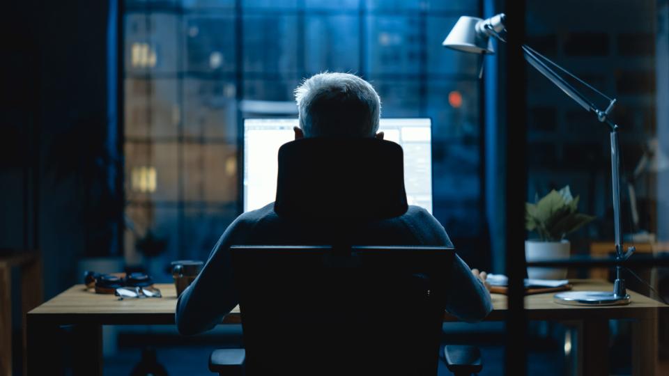 A remote worker looking at his computer in a dark room