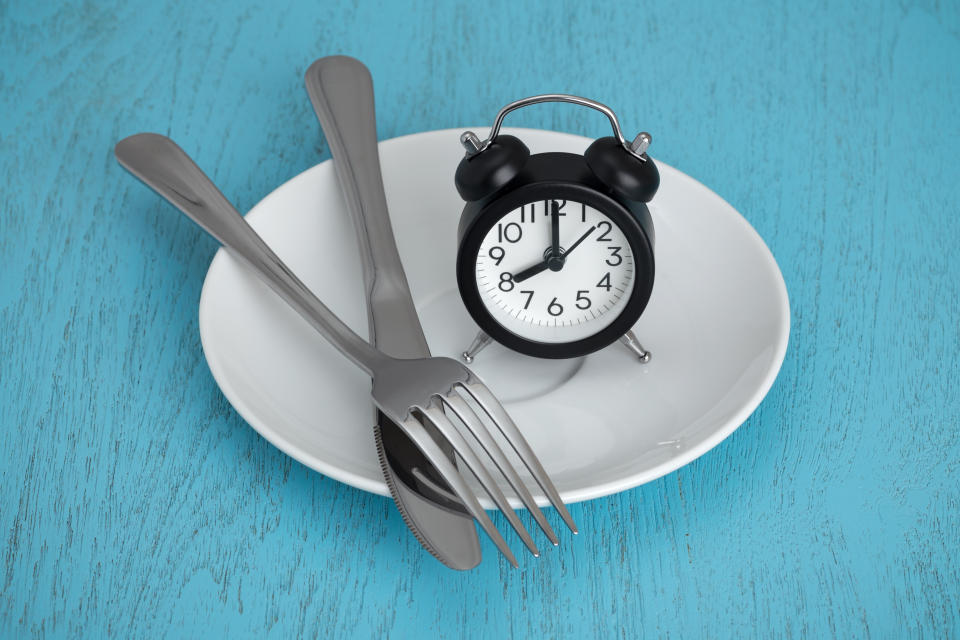 Intermittent fasting concept with clock on white plate, fork and knife on blue table