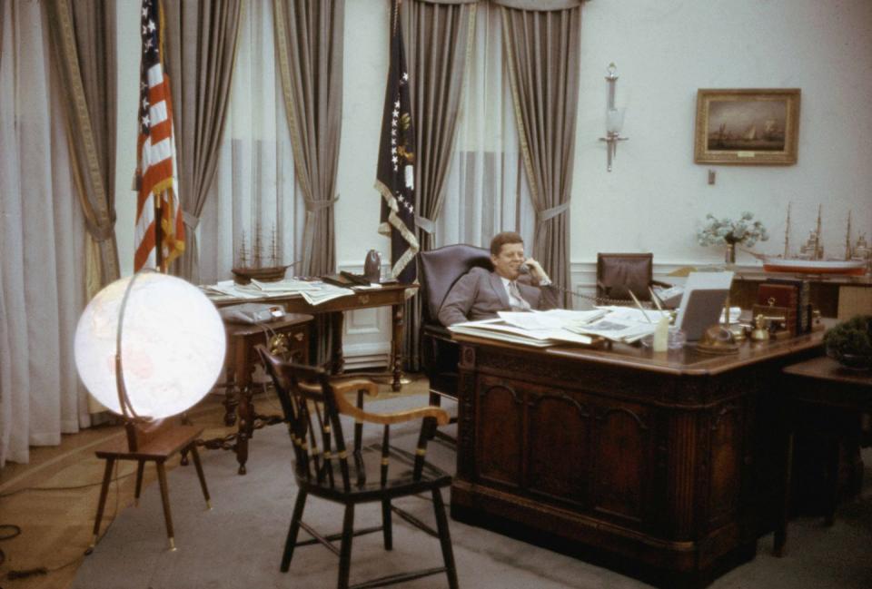 <p>President John F. Kennedy smiles as he speaks on the phone in the Oval Office.</p>