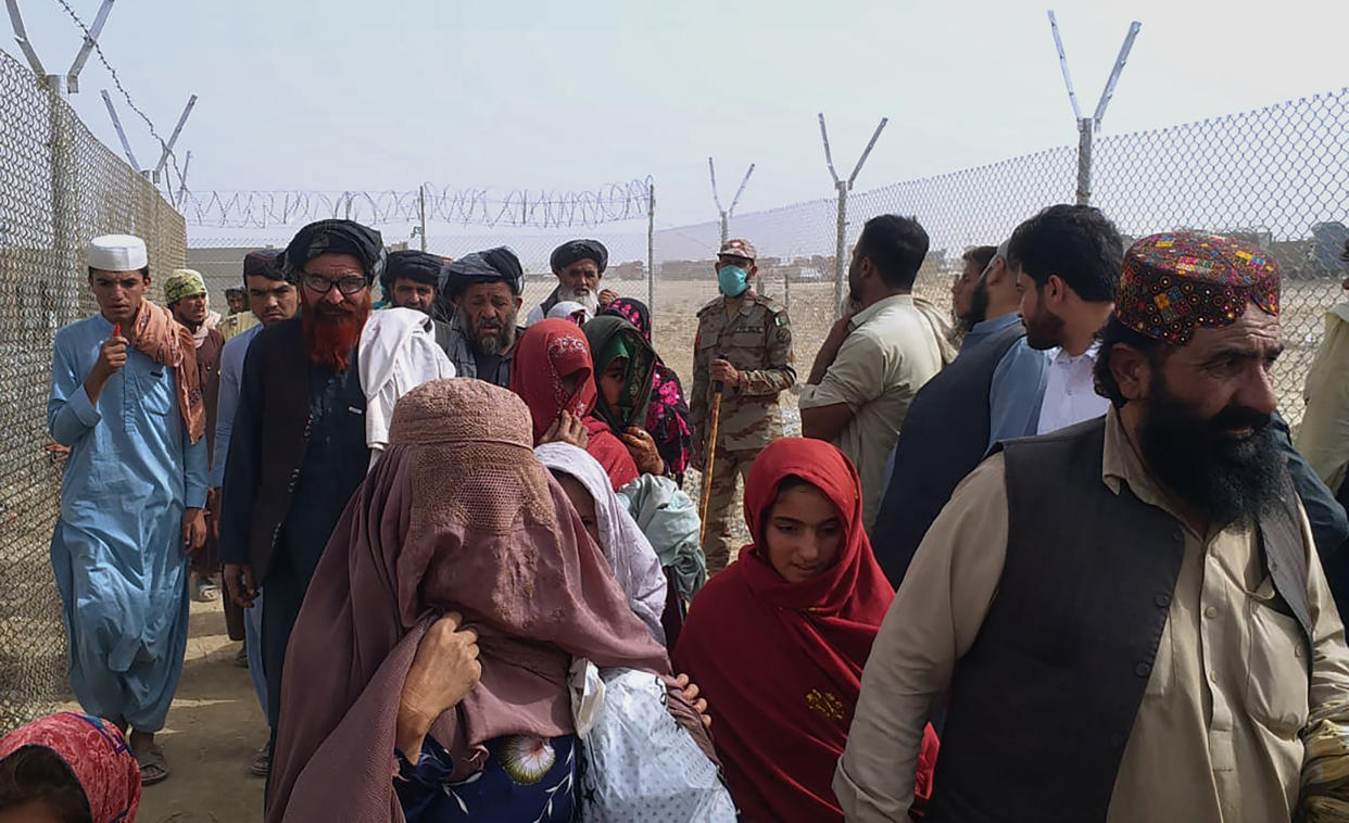 People walk through a security barrier while they enter Pakistan through a border crossing point, in Chaman, Pakistan, Monday, Aug. 16, 2021. Normally thousands of Afghans and Pakistanis cross daily and a steady stream of trucks passes through, taking goods to land-locked Afghanistan from the Arabian Sea port city of Karachi in Pakistan.(AP Photo/Jafar Khan)