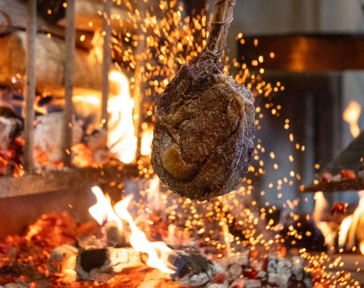 A tomahawk steak cooks over an open fire at the Little West Tavern in the Junto.