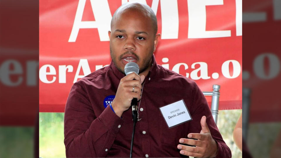 Devin R. Jones holds a microphone as he speaks.