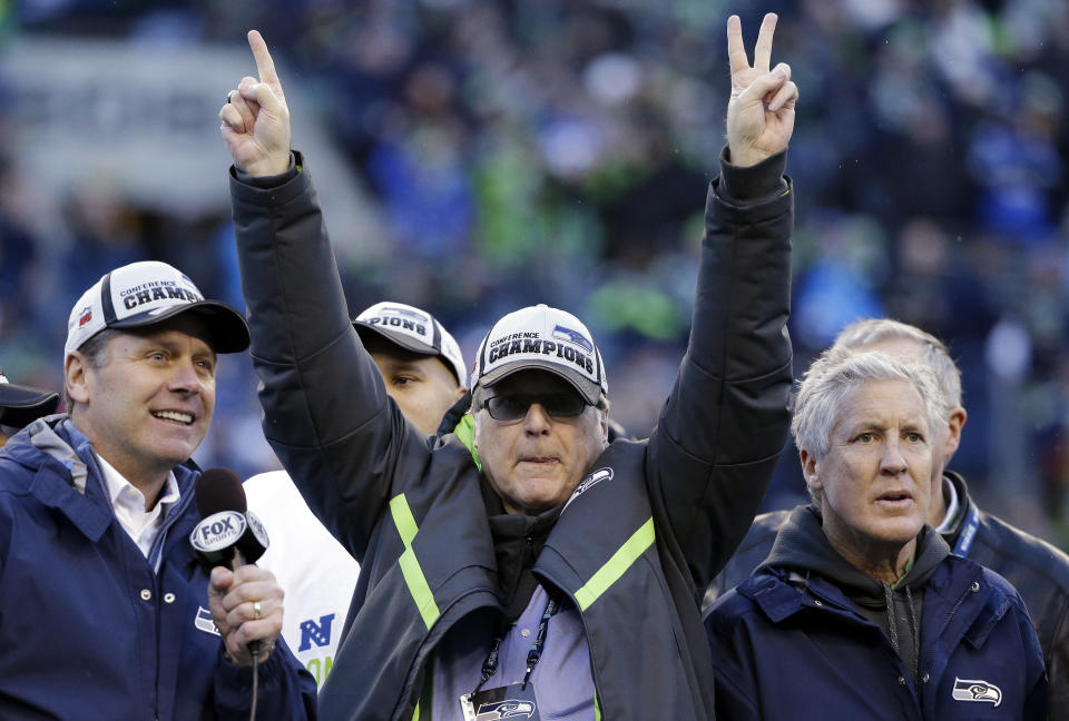 ARCHIVO - En esta foto de archivo del 18 de enero de 2015, Paul Allen (centro), dueño de los Seahawks de Seattle, marca con los dedos el número 12, para agradecer el apoyo de los fanáticos tras una victoria sobre los Packers de Green Bay en la final de la Conferencia Nacional (AP Foto/Elaine Thompson, archivo)