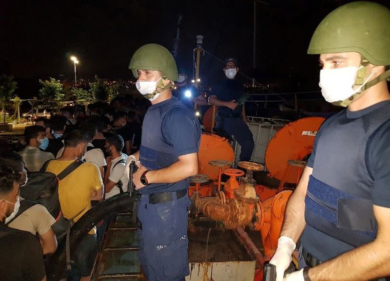 Members of Turkish Coast Guard Command stand guard next to migrants on the deck of a cargo ship during a raid in Izmir