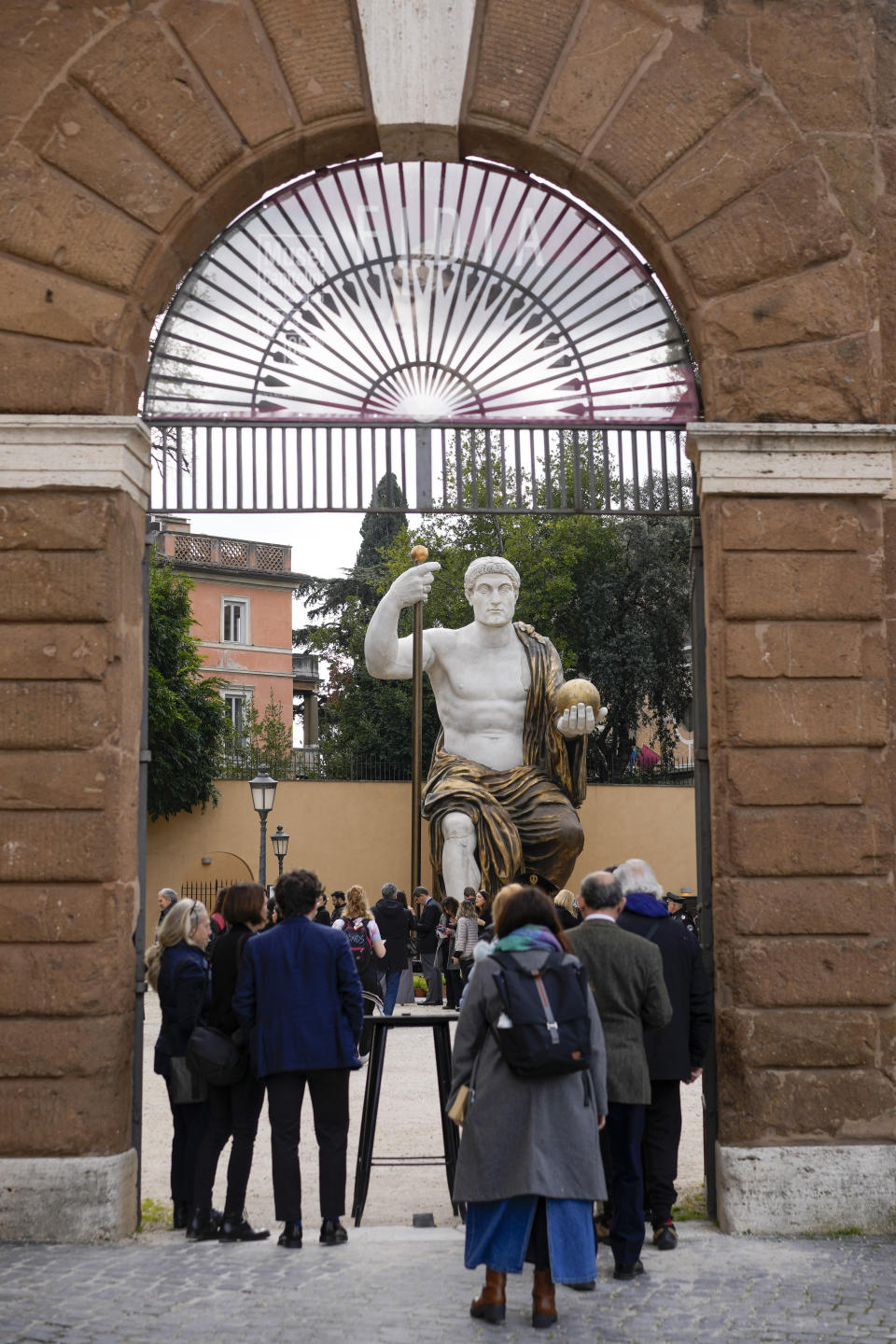 Visitors admire a massive, 13-meter (yard) replica of the statue Roman Emperor Constantine commissioned for himself after 312 AD that was built using 3D technology from scans of the nine giant original marble body parts that remain, as it was unveiled in Rome, Tuesday, Feb. 6, 2024. The imposing figure of a seated emperor, draped in a gilded tunic and holding a scepter and orb, gazing out over his Rome, is located in a side garden of the Capitoline Museums, just around the corner from the courtyard where the original fragments of Constantine's giant feet, hands and head are prime tourist attractions. (AP Photo/Andrew Medichini)