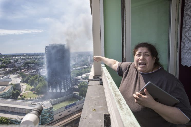 Eine Frau steht auf dem Balkon und deutet panisch auf das brennende Gebäude (Bild: AP)