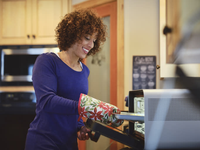 Woman smiling and  taking a baking sheet out of toaster oven