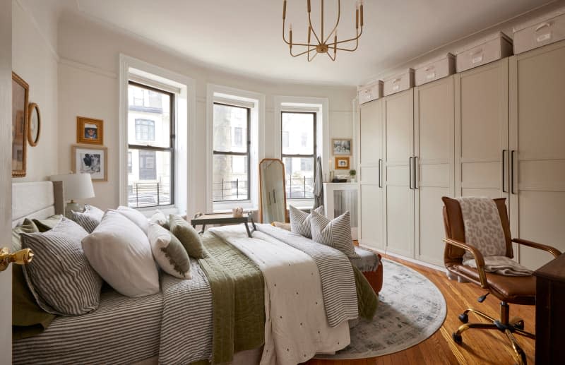 Chandelier hangs above bed with lots of bedding and pillows in bedroom with wall of storage.