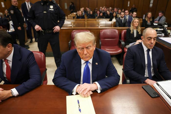 Donald Trump sentado con una libreta dentro de la sala del tribunal, flanqueado por dos hombres