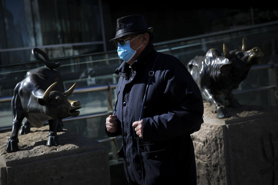 A man wearing a protective face mask walks by statues of bulls on display outside a bank in Beijing, Tuesday, March 10, 2020. Asian stock markets took a breather from recent steep declines on Tuesday, with several regional benchmarks gaining more than 1% after New York futures reversed on news that President Donald Trump plans to ask Congress for a tax cut and other quick measures to ease the pain of the virus outbreak. (AP Photo/Andy Wong)