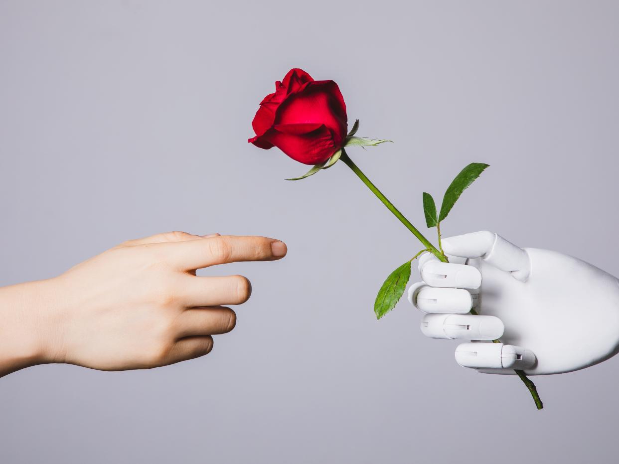 Human hand reaching for red rose in robotic hand
