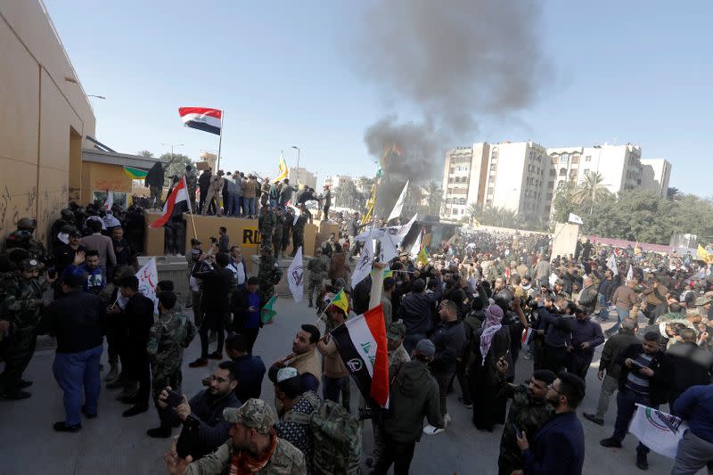 Protesters and militia fighters gather to condemn air strikes on bases belonging to Hashd al-Shaabi, outside the main gate of the U.S. Embassy in Baghdad