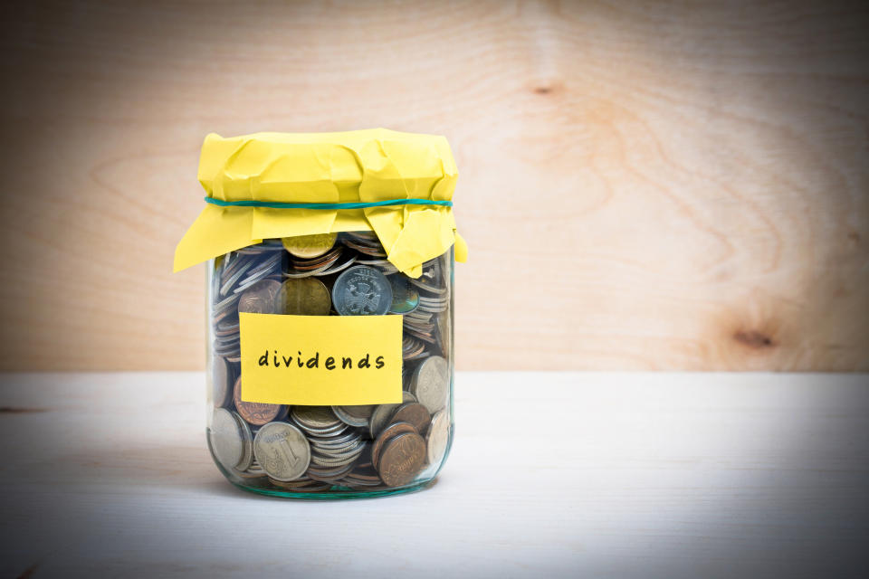 A jar full of coins, marked dividends, with yellow paper as lid holding it closed by a rubber band.