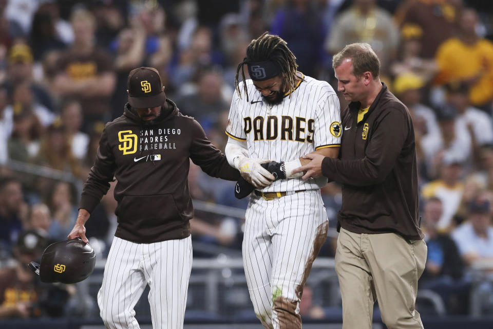 San Diego Padres' Fernando Tatis Jr., center, is helped off the field by manager Jayce Tingler, left, and a trainer during the first inning of the team's baseball game against the Colorado Rockies, Friday, July 30, 2021, in San Diego. (AP Photo/Derrick Tuskan)