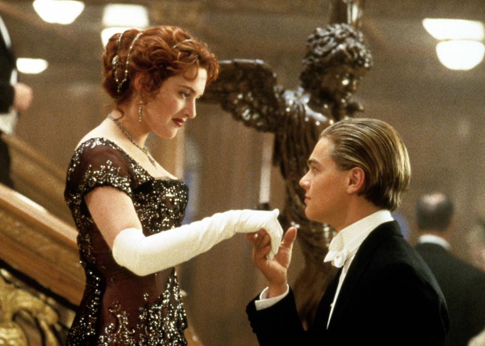 A man in a tuxedo kisses the hand of a woman in an embellished gown on the Titanic's grand staircase