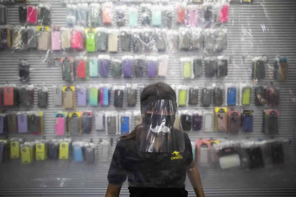 A woman wearing a protective face mask and face shield, stands behind of a plastic sheet set up as a measure to curb the spread of the new coronavirus, at a cell phone technology store in Caracas, Venezuela, Friday, June 5, 2020. President Nicolas Maduro and Venezuela's opposition, led by Juan Guaido, have agreed to measures for battling the new coronavirus to be overseen by international health workers, a first step in years toward cooperation between bitter political rivals for the benefit of the country. (AP Photo/Ariana Cubillos)