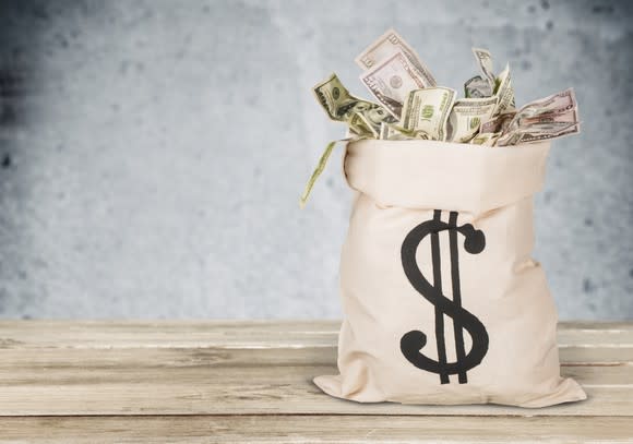 A burlap sack overflowing with paper currency sits on a table.