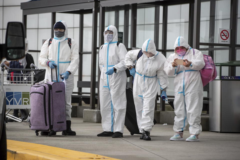 People wearing protective face masks, goggles and Tyvek suits, who said they traveled from Colombia wait for a car rental company shuttle, after arriving at Vancouver International Airport in Richmond, British Columbia., Thursday, Dec. 31, 2020. Beginning January 7, air travelers arriving in Canada will be required to provide proof of a negative COVID-19 test conducted within 72 hours of boarding the plane. (Darryl Dyck/The Canadian Press via AP)