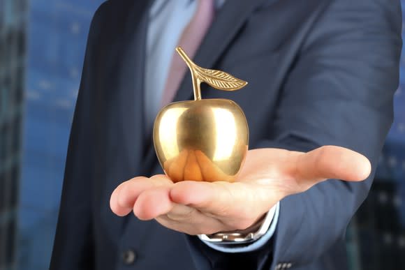 Businessman holding up a golden apple in the palm of his outstretched hand.