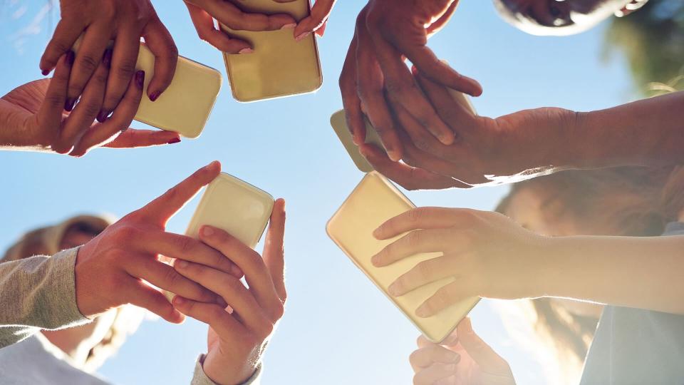 Cropped shot of a group of friends using their phones together outdoors.