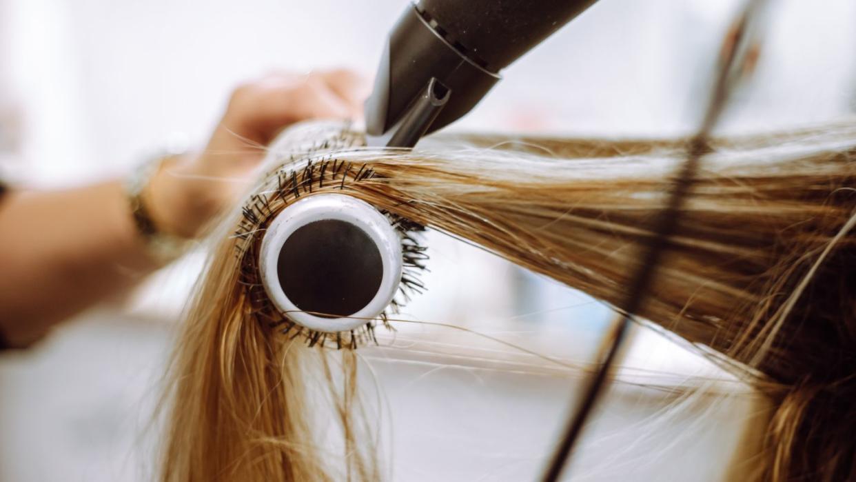 close up view of lock of long blond hair on hairbrush being dried by blow dryer