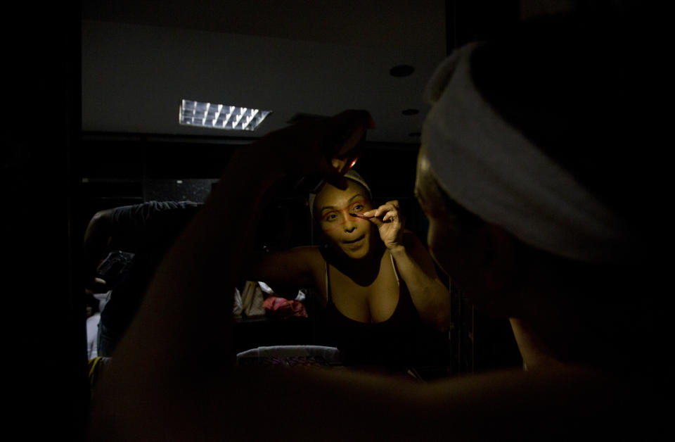 In this Dec. 4, 2018 photo, dancer Morelis Silva uses a cell phone to provide illumination to apply makeup in preparation for the contemporary dance production Ubuntu, at the Teresa Carreno Theater in Caracas, Venezuela. (AP Photo/Fernando Llano)
