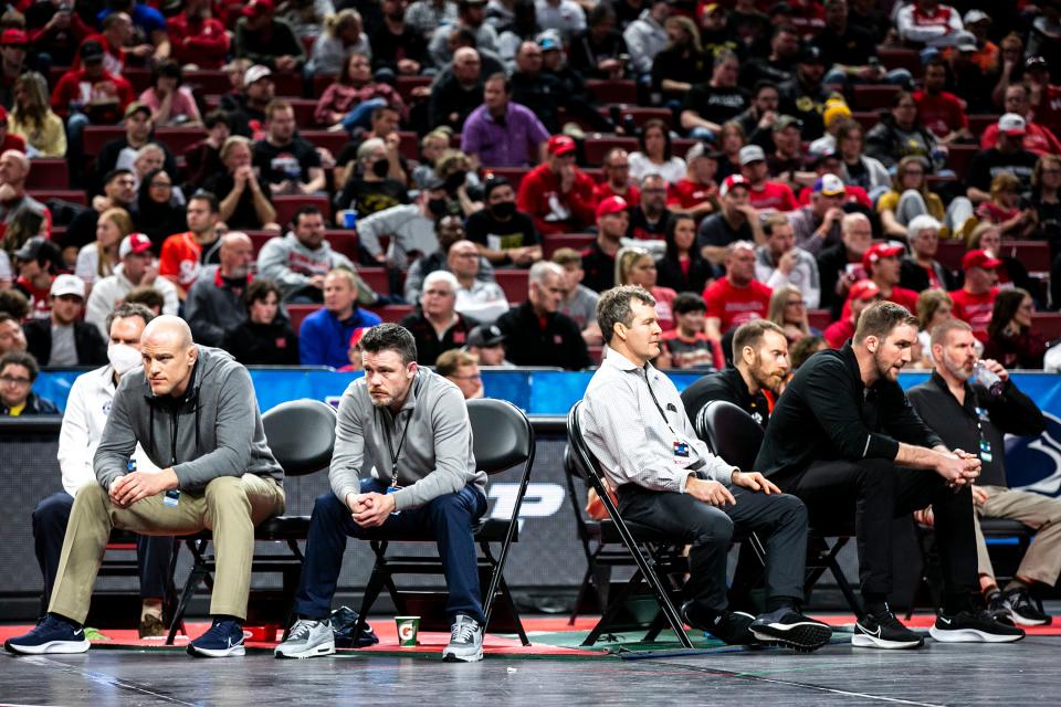 Penn State coaches, left, and Iowa coaches, right, sit next to each other on different mats at the 2022 Big Ten Championships in Lincoln, Neb. The Hawkeyes and Nittany Lions wrestle each other on Friday.