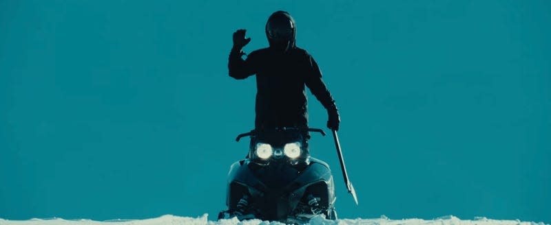 A figure waves from a snowmobile, holding an axe