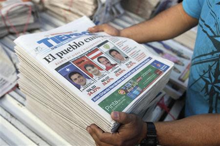 A vendor arranges newspapers covering the preliminary tally of presidential candidates Juan Orlando Hernandez of the National Party and Xiomara Castro of the Liberty and Refoundation Party (LIBRE) on the front page, in Tegucigalpa November 25, 2013. REUTERS/Jorge Cabrera