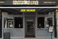 Shao Lin Tia, left, and her husband, Christophe Tia, look out from the window of their second Thai restaurant on Rue Daguerre in Paris on May 2, 2020, as they wait for takeout customers. About five weeks into France's nationwide confinement to slow the spread of the coronavirus, the couple were allowed to open for a limited takeout business. In recent weeks, they have added a few outdoor tables, but sales remain low and Shao Lin worries that the hardest is yet to come. (AP Photo/Francois Mori)