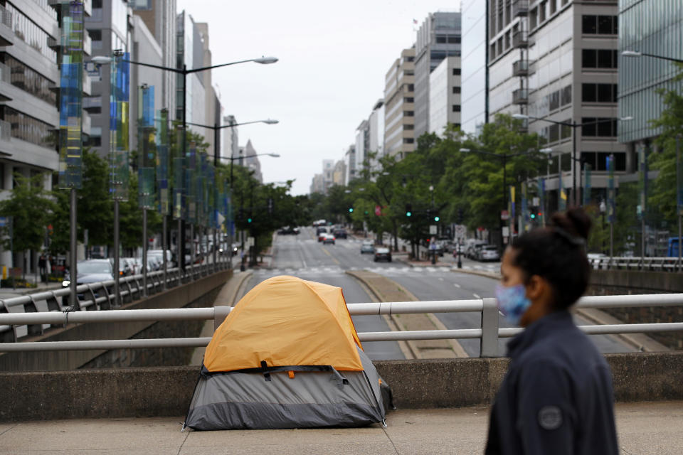 A homeless person's tent sits above a quiet K Street Northwest as a woman wearing a face mask to protect against the spread of the new coronavirus walks past, Thursday, May 21, 2020, in Washington. The District of Columbia is under a stay-home order for all residents in an effort to slow the spread of the new coronavirus. (AP Photo/Patrick Semansky)