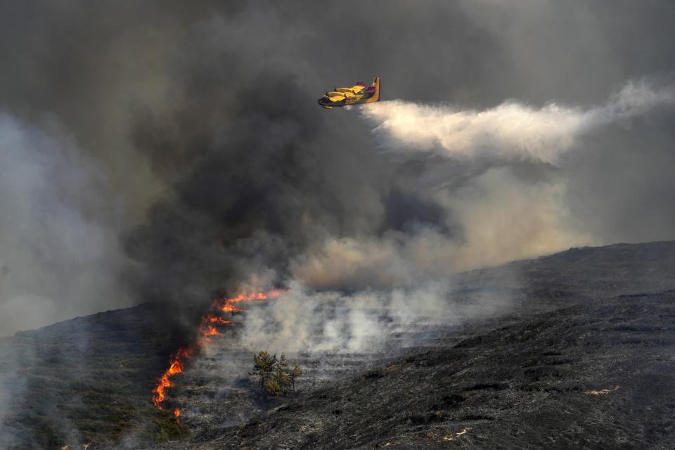 A Canadair aircraft drops water over a wildfire in Vati village, on the Aegean Sea island of Rhodes, southeastern Greece, on Tuesday, July 25, 2023. A third successive heat wave in Greece pushed temperatures back above 40 degrees Celsius (104 degrees Fahrenheit) across parts of the country Tuesday following more nighttime evacuations from fires that have raged out of control for days. (AP Photo/Petros Giannakouris)