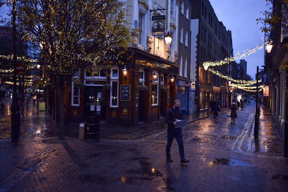 A man wears a face mask as he walks past a closed pub in the Seven Dials area of Covent Garden, in London, Wednesday, Dec. 16, 2020. The consensus across the four nations of the U.K. over the planned easing of coronavirus restrictions over Christmas appears to be fraying — even though they all agreed Wednesday to keep in place the laws around the relaxation. (AP Photo/Alberto Pezzali)