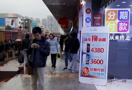 A man checks his smartphone outside a store promoting the Apple iPhone products in the southern Chinese city of Shenzhen, January 26, 2016. Chinese characters on the iPhone-shape advertisement board read "New year change new phone" (top) and "Installment. Old for new". REUTERS/Bobby Yip