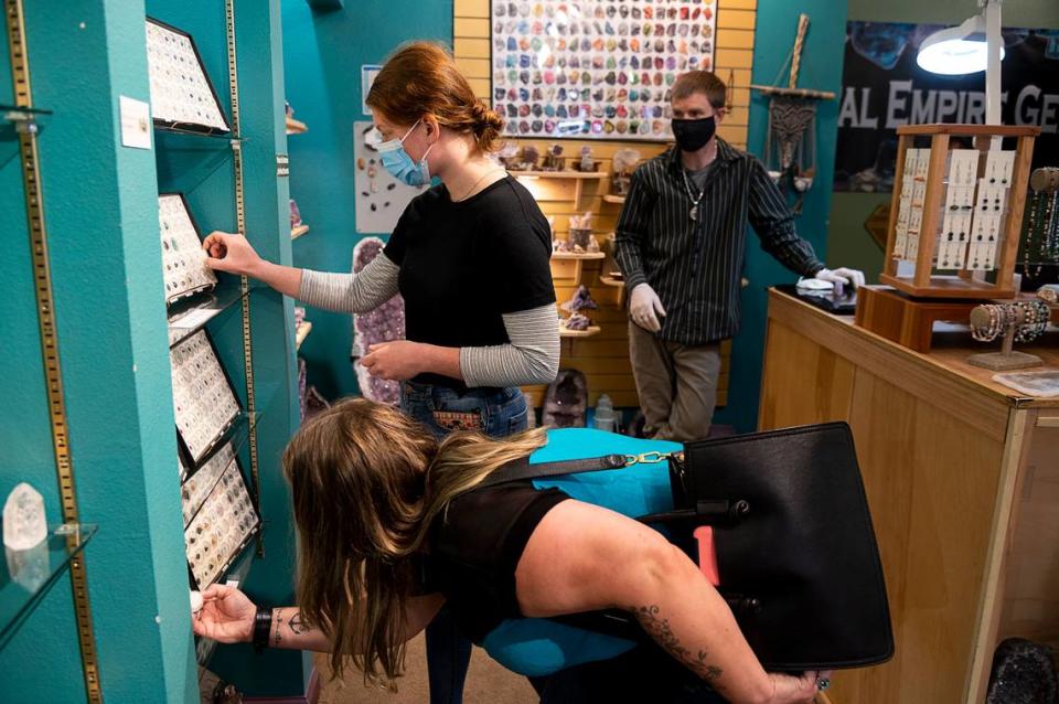 James Hill, right, owner of Crystal Empire Gems, wears a mask as he helps customers Alison Hertz and her niece Kelci Anderson shop on Monday, May 18, 2020 in Grass Valley during the coronavirus pandemic.