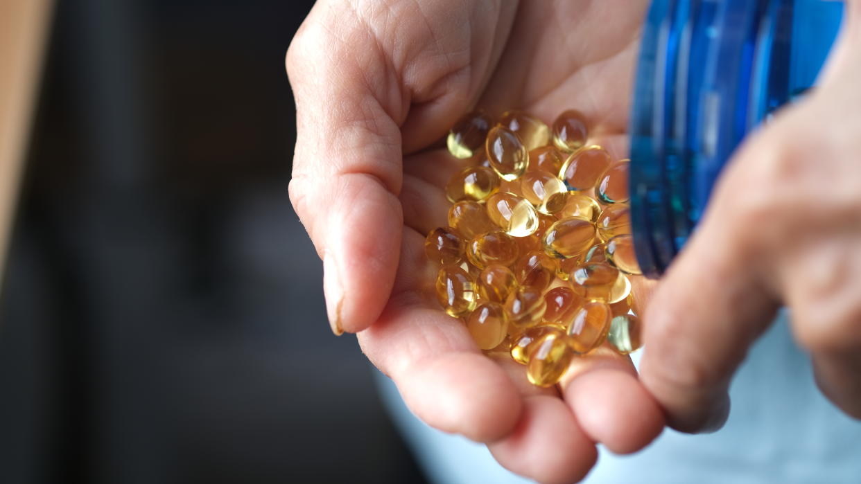  Close up on an older person's hands as they pour out a large quantity of soft gel vitamins into their palm. 