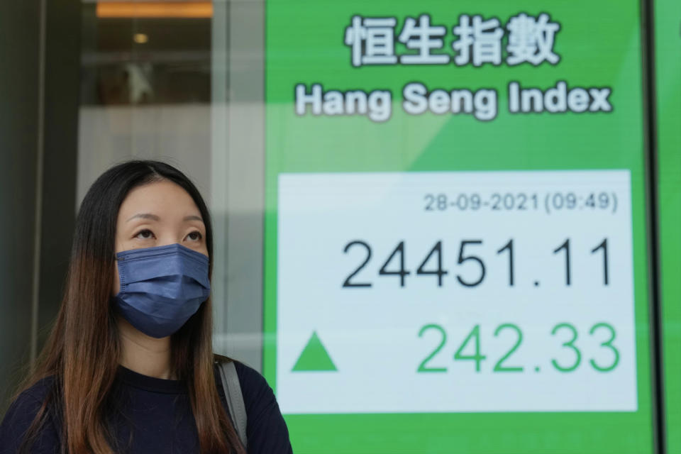 A woman wearing a face mask walks past a bank's electronic board showing the Hong Kong share index in Hong Kong, Tuesday, Sept. 28, 2021. Asian shares mostly fell Tuesday as concerns about China chipped away at investor optimism following a mixed finish on Wall Street. (AP Photo/Kin Cheung)