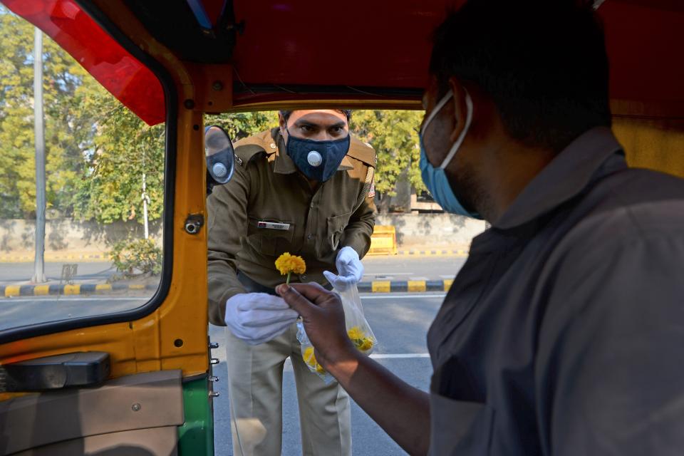 A policeman gives a flower to an auto rickshaw driver in a bid to inspire him to stay home during a one-day Janata (civil) curfew imposed as a preventive measure against the COVID-19 coronavirus, in New Delhi on March 22, 2020. - Nearly one billion people around the world were confined to their homes, as the coronavirus death toll crossed 13,000 and factories were shut in worst-hit Italy after another single-day fatalities record. (Photo by Sajjad HUSSAIN / AFP) (Photo by SAJJAD HUSSAIN/AFP via Getty Images)