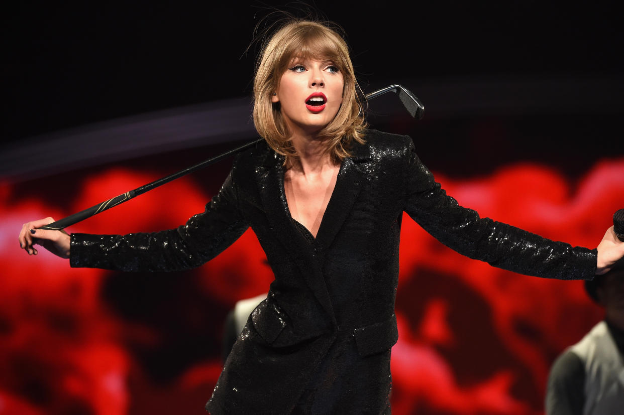 Taylor Swift, wearing a sparkly jacket, casually holds a golf club.