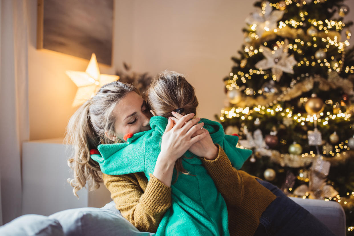 Little girl and her mom on Christmas morning at home. Girl is sad about something and mother is hugging her.