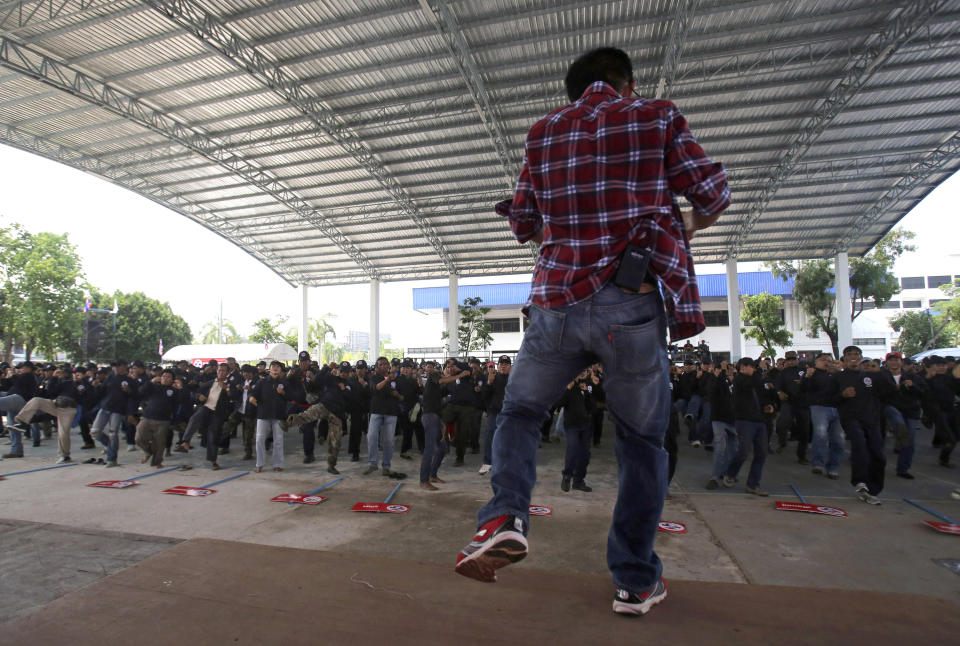 In this April 3, 2014 photo, a trainer directs black-clad supporters of Thai Prime Minister Yingluck Shinawatra during a Thai kickboxing exercise in Udon Thani province, Thailand. Following the directions of the trainer on a nearby stage, they fended off kicks and practiced footwork to loud speakers blaring music typically heard at a Thai kickboxing stadium. It was was part of a two-day training course for farmers, laborers and others in the heart of pro-government “Red Shirt” country - Thailand’s rural, poor north and northeast. (AP Photo/Sakchai Lalit)