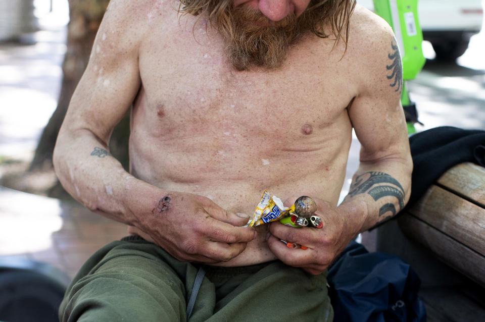 A man holding a glass pipe and two lighters struggles to wrestle a piece of candy from a wrapper while sitting on a bench in downtown Portland, Ore. on Thursday, May 18, 2023. Three years ago, nearly two-thirds of Oregon voters approved a ballot measure decriminalizing illicit drugs, backing the idea that addiction treatment is more effective than jail. But now, public drug use in cities such as Portland and a surge in fentanyl overdose deaths have created a backlash against the first-in-the-nation law. (Beth Nakamura/The Oregonian via AP)